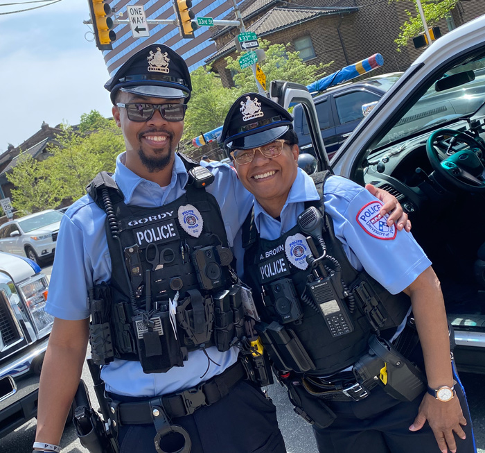two officers pose in front of a police car